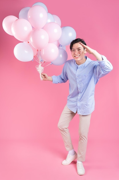 Junger asiatischer Mann, der Ballon auf rosa Hintergrund hält