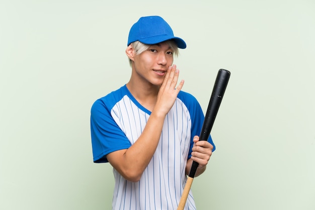 Junger asiatischer Mann, der Baseball über dem lokalisierten Grün flüstert etwas spielt