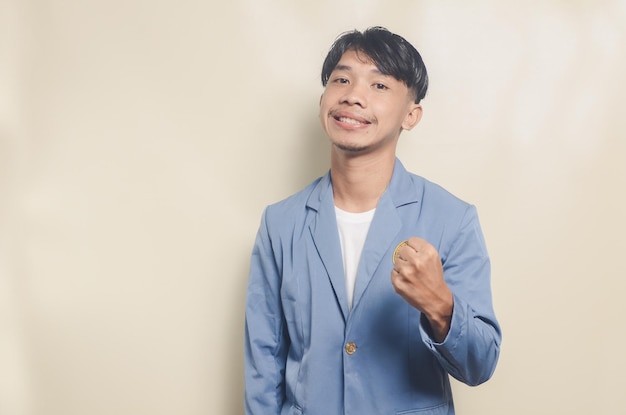 Junger asiatischer mann, der college-anzug mit aufgeregtem ausdruck trägt