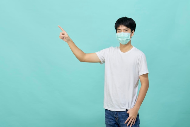 Junger asiatischer Mann, der ein medizinisches Gesichtsmasken-T-Shirt trägt, das auf leeren Raum mit Blick auf die Kamera steht