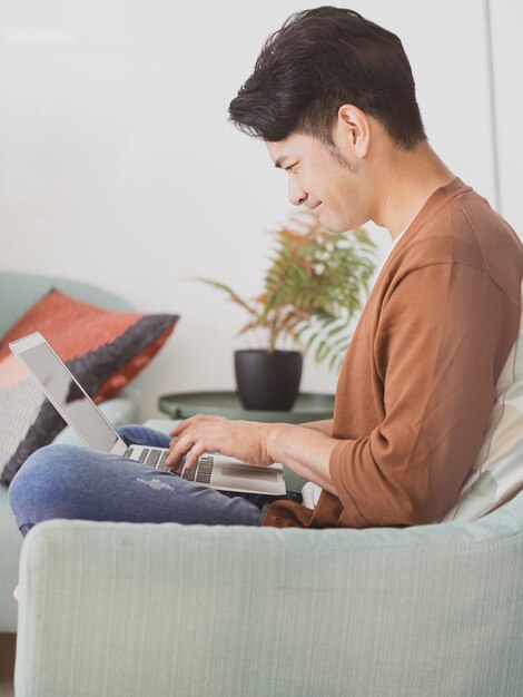 Junger asiatischer Mann, der Freizeitkleidung trägt und Laptop benutzt