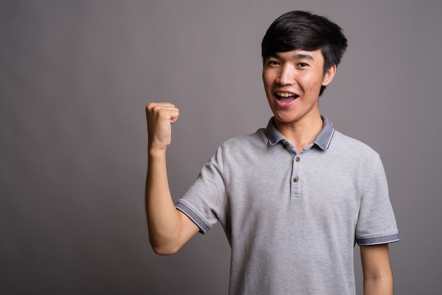 Junger asiatischer Mann, der graues Poloshirt gegen graue Wand trägt