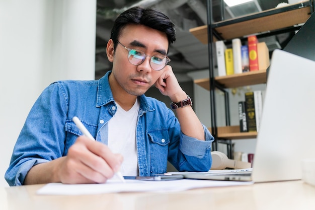 Junger asiatischer Mann, der im Büro arbeitet