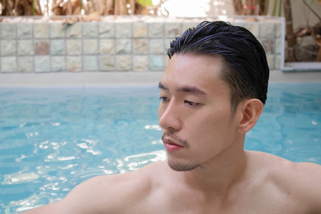 Junger asiatischer Mann, der im Schwimmbad im Urlaub steht.