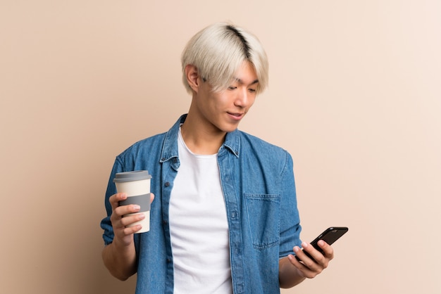 Junger asiatischer Mann, der Kaffee hält, um und ein Mobile wegzunehmen