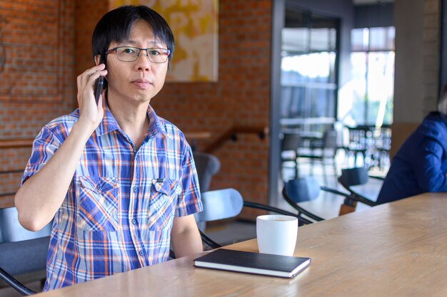 Junger asiatischer Mann, der Kaffee im Café trinkt und Smartphone verwendet