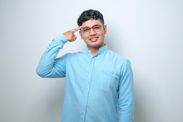 Junger asiatischer mann, der lässiges hemd trägt, das lächelt und mit beiden händen auf den kopf zeigt, finger große idee oder gedanke