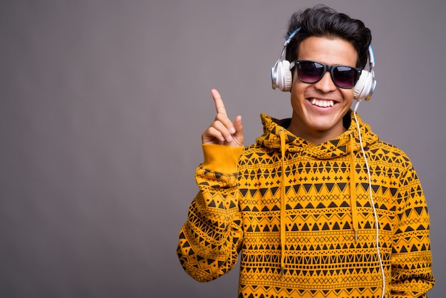 junger asiatischer Mann, der Musik hört, während er Hoodie gegen graue Wand trägt