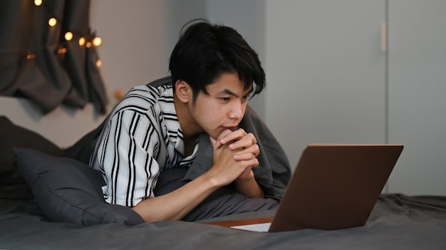 Junger asiatischer Mann, der nachts mit Computerlaptop im Internet surft.