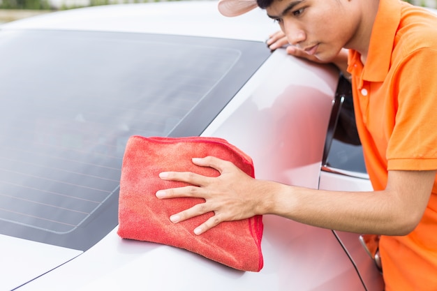 Junger asiatischer Mann, der roten microfiber Stoffreinigungskörper des neuen silbernen Autos verwendet