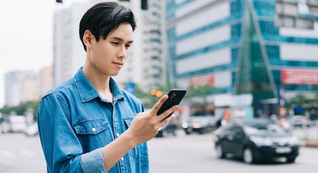 Junger asiatischer Mann, der Smartphone auf der Straße geht und verwendet
