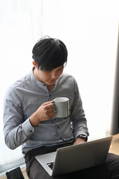 Junger asiatischer Mann, der von zu Hause auf einem Laptop arbeitet