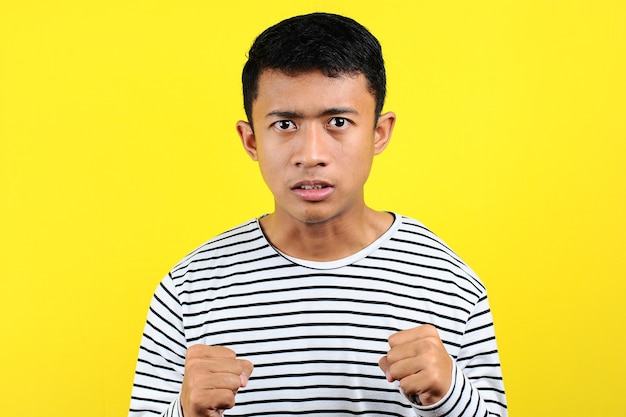 Junger asiatischer Mann, der wütende Geste macht, verärgert und emotional, isoliert auf gelbem Hintergrund