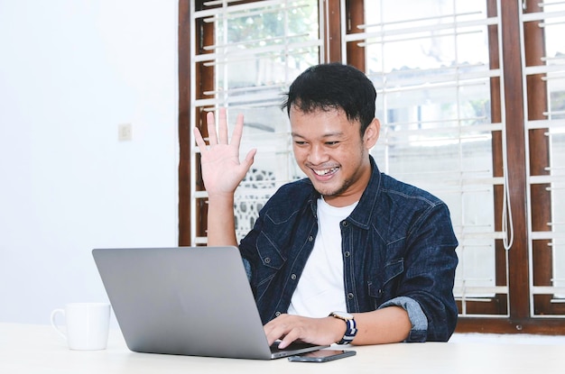 Junger asiatischer Mann glücklich und aufgeregt bei Videoanruf mit Laptop auf dem Tisch