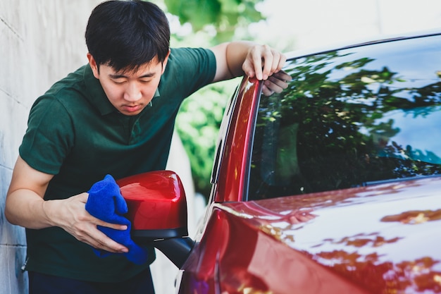 Junger asiatischer Mann in der Uniform, die ein Auto in im Freien säubert und wäscht