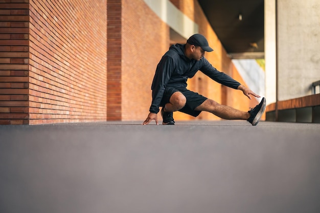 Junger asiatischer Mann in Sportbekleidung, der im Freien läuft Porträts eines indischen Mannes, der sich das Bein streckt, bevor er auf der Straße läuft Trainingssportler trainieren im Outdoor-Konzept