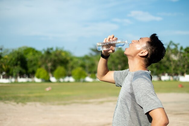 Junger asiatischer Mann in Sportbekleidung Trinkwasser nach seinem Training