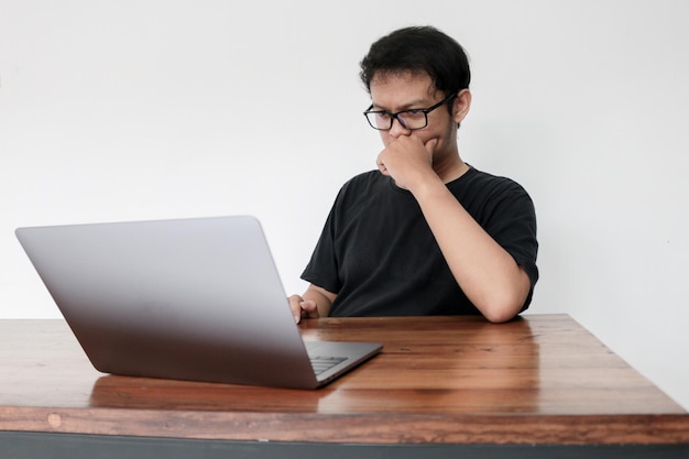 Junger asiatischer Mann ist ernsthafte Arbeit oder denkt an der Vorderseite des Laptops Indonesien Mann trägt schwarzes Hemd Isolierter grauer Hintergrund