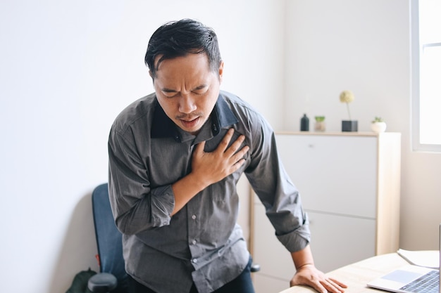 Junger asiatischer Mann leidet an Herzinfarkt am Schreibtisch