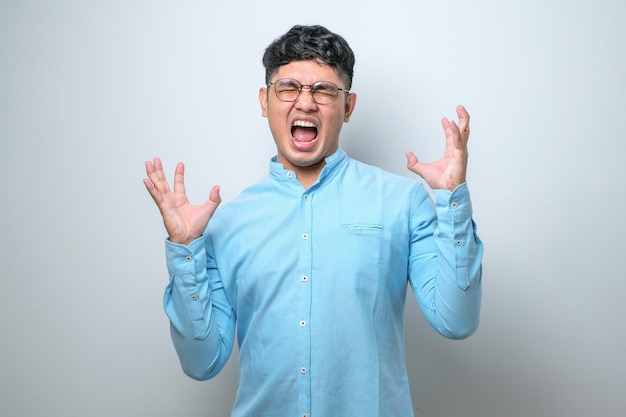 Junger asiatischer Mann mit Freizeithemd verrückt und wütend schreien und schreien mit aggressivem Ausdruck und erhobenen Armen Frustrationskonzept