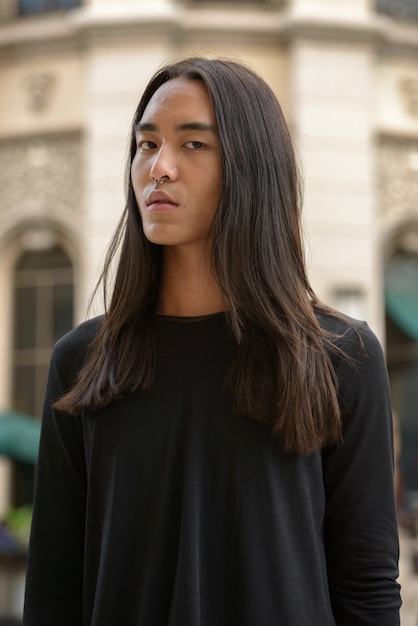 Junger asiatischer Mann mit langen Haaren in der Stadt