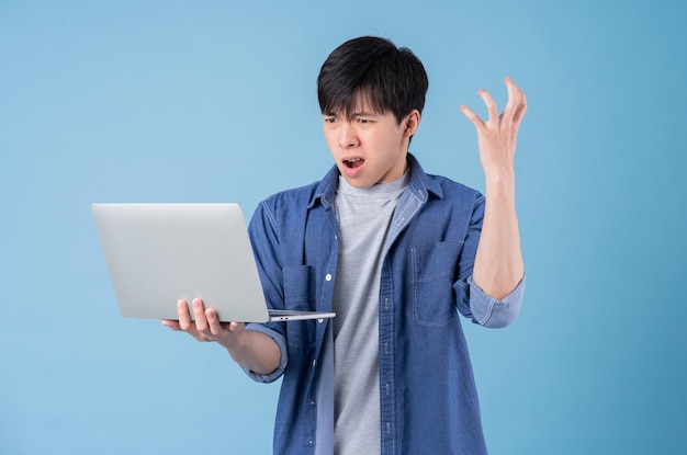 Junger asiatischer Mann mit Laptop auf blauem Hintergrund