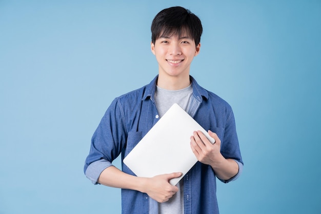 Junger asiatischer Mann mit Laptop auf blauem Hintergrund