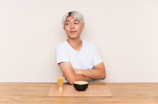 Junger asiatischer Mann mit matcha Tee in einem Tabellenlachen