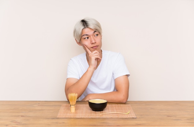 Junger asiatischer Mann mit matcha Tee in einer Tabelle eine Idee denkend