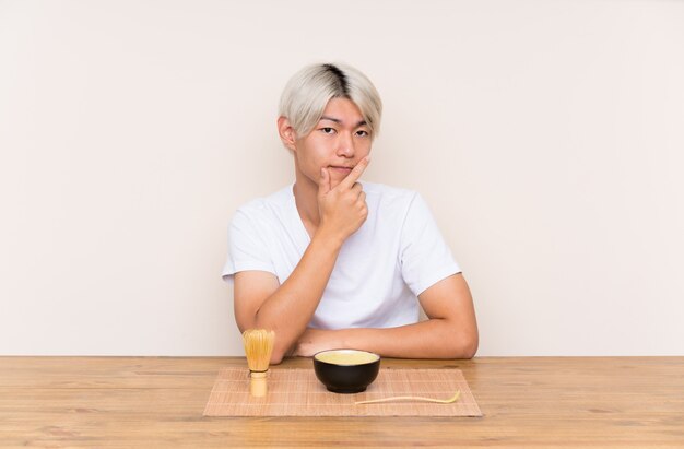 Junger asiatischer Mann mit matcha Tee in einer Tabelle eine Idee denkend