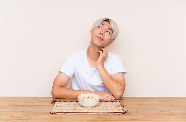 Junger asiatischer Mann mit Ramen in einer Tabelle eine Idee denkend