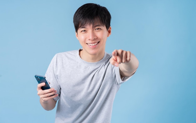 Junger asiatischer Mann mit Smartphone auf blauem Hintergrund