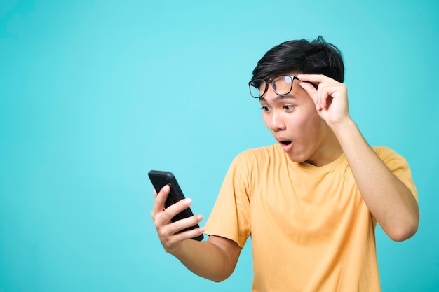 Junger asiatischer Mann mit überraschtem Gesichtsausdruck hält Smartphone in seinen Händen
