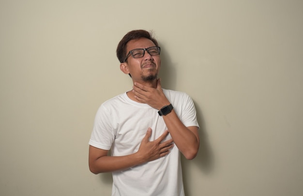 Junger asiatischer Mann mit weißem Hemd, der schmerzhafte Halsschmerzen für Grippeklumpen und Infektionen berührt