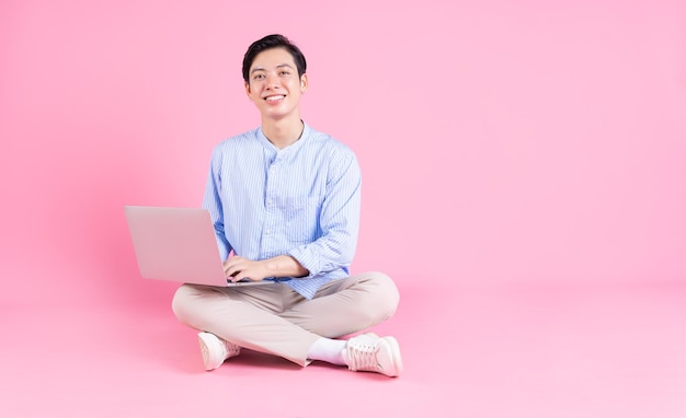 Junger asiatischer Mann sitzt und benutzt Laptop im Hintergrund