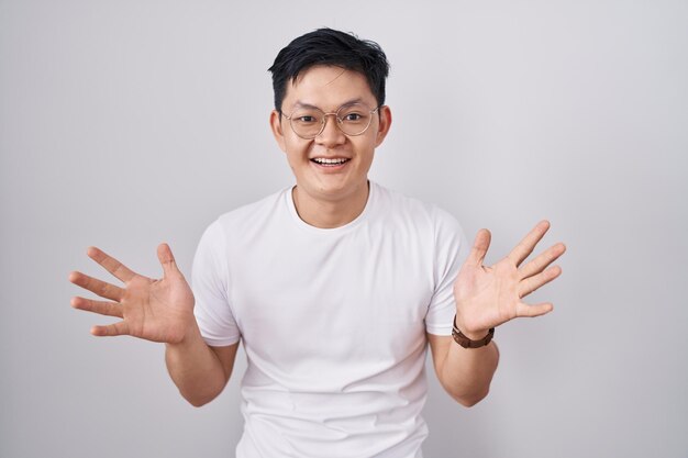 Junger asiatischer Mann steht vor weißem Hintergrund und feiert verrückt und erstaunt über den Erfolg mit erhobenen Armen und offenen Augen und schreit aufgeregt über das Siegerkonzept