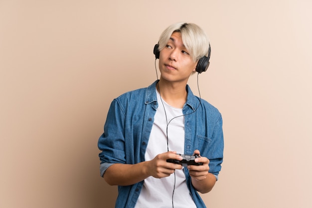 Junger asiatischer Mann über dem lokalisierten Hintergrund, der an den Videospielen spielt