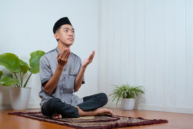 Junger asiatischer muslimischer Mann betet auf dem Gebetsteppich zu Hause auf Ramadan Kareem