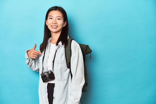 Foto junger asiatischer reisender, der bereit ist, abenteuer einzufangen, person, die mit der hand auf einen kopierraum für ein hemd zeigt