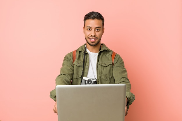 Junger asiatischer Reisendmann, der einen Laptop hält