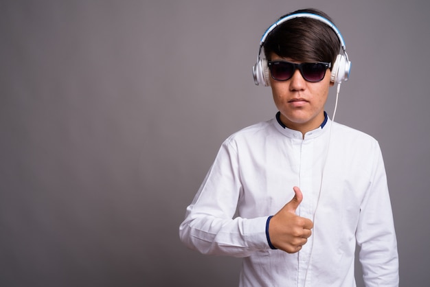 junger asiatischer Teenager, der Musik vor grauem Hintergrund hört