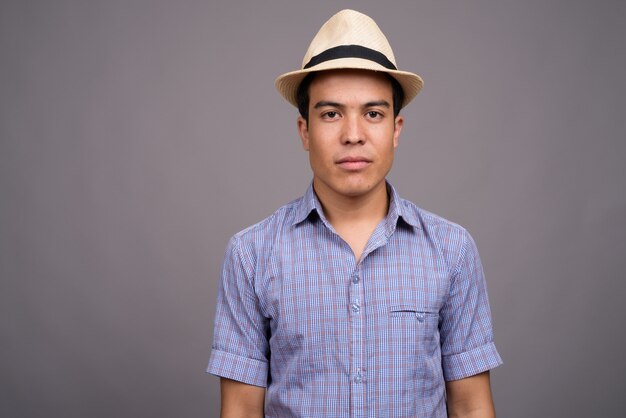 junger asiatischer Touristenmann, der Hut bereit für Urlaub gegen graue Wand trägt