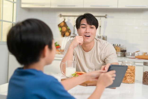 Junger asiatischer Vater und sein Sohn mit digitalem Tablet genießen gemeinsam in der Küche zu Hause