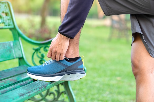 Junger Athletenmann, der Laufschuhe im Park im Freien bindet