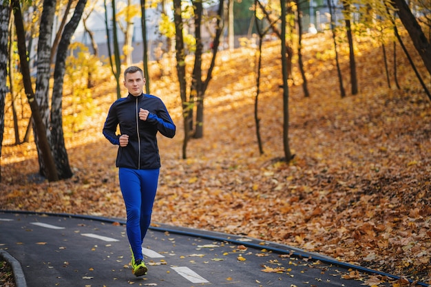 Junger athletischer Mann, der am Park während des Herbstmorgens läuft