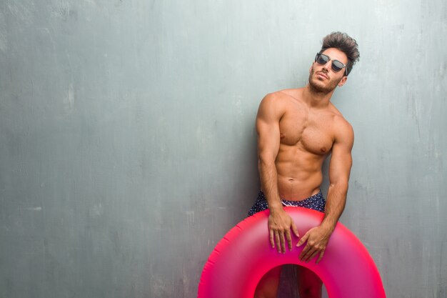 Junger athletischer Mann, der einen Badeanzug gegen eine grunge Wand oben schaut trägt