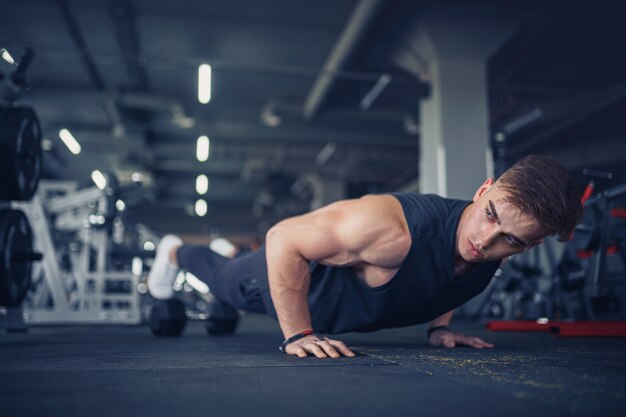 Junger athletischer Mann, der Liegestütze im Fitnessstudio tut