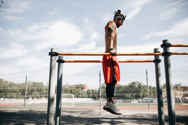 Junger athletischer Mann macht einen Handstand am Stufenbarren auf dem Sportplatz draußen