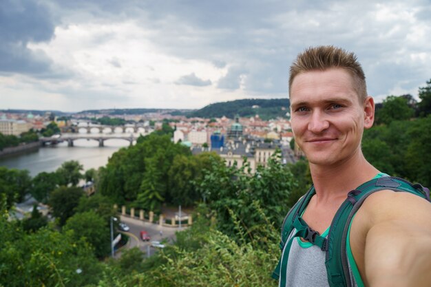 Foto junger attraktiver kerl, der selfie mit landschaftsblickbrücken auf moldau in der tschechischen republik prag nimmt.