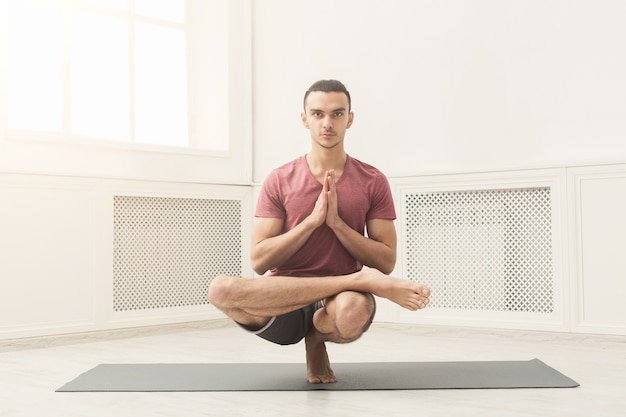 Junger attraktiver Mann, der Yoga praktiziert, Gleichgewichtsübungen auf der Matte im Fitnesskurs macht, Vorderansicht, Kopierraum